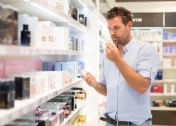 Elegant man choosing perfume in retail store. Casual man testing and buying gift for his lady in a beauty store.