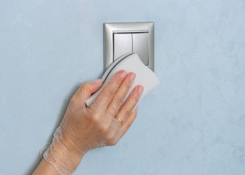 Woman hand in vinyl glove is cleaning the light switch on blue wall by melamine sponge. Cleaning and disinfecting concept