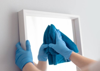 Woman cleaning mirror with blue napkin from pollution and plaque from water at home