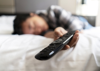 girl sleeping on hotel bed, holding TV remote control