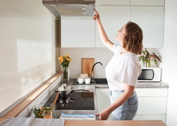 Cropped view of woman select mode on cooking hood, standing near kitchen appliance in modern interior house with house plants in flower pot on hobs. Stock photo