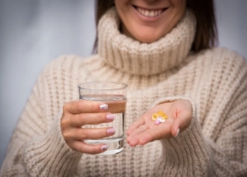 Young beautiful smiling woman holding multivitamins and supplements and a glass of water. Vitamin K2, D, E, A and fish oil capsules. High quality photo