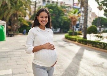 Young latin woman pregnant smiling confident touching belly at street
