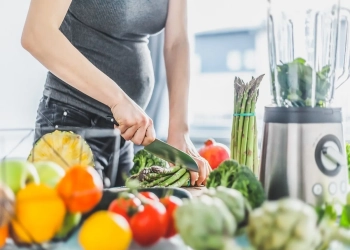 Young pregnant woman cooking healthy meal food vegetables in the kitchen. Lifestyle background. Horizontal