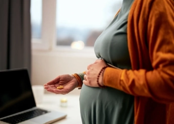 Cutout picture of pregnant caucasian businesswoman standing in office, touching belly and holding pill.