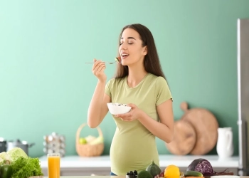 Young pregnant woman eating fresh vegetable salad in kitchen